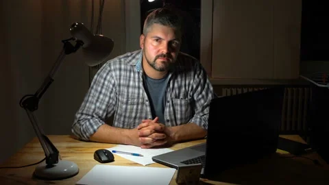 Bearded man sits at a table with a lit lamp 4K Video stock 130148748