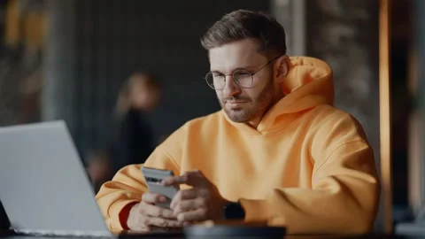 Bearded Man Sitting Alone In Cafe, Using Mobile Phone And Laptop, Freelancer Stock-Footage 343669016