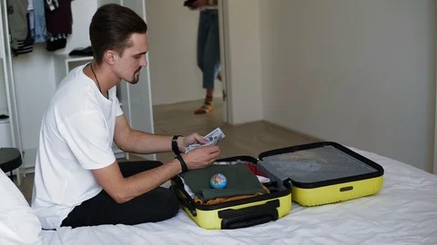 Bearded man is sitting on bed, preparing for vacation - US dollars notes - man Stock Footage 123205501