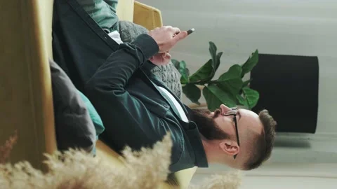 Bearded man sitting on couch at home chatting, typing message using cellular. Stock Footage 156327728