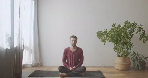 Bearded man sitting cross-legged on yoga mat practicing pranayama with closed Stock Footage 140662412