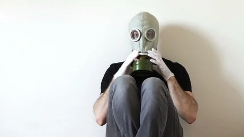 Bearded man is sitting on ground removing his gas mask Stock Footage 127489697