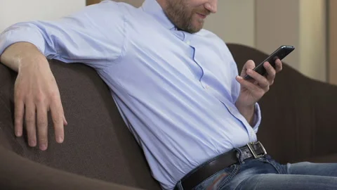 Bearded man sitting on sofa and scrolling smartphone, social networks, gadget Stock Footage 86781993