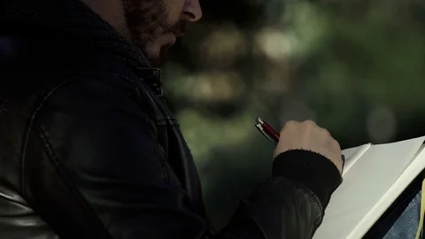 Bearded man sitting under a tree writing in a notebook Video stock 71931027