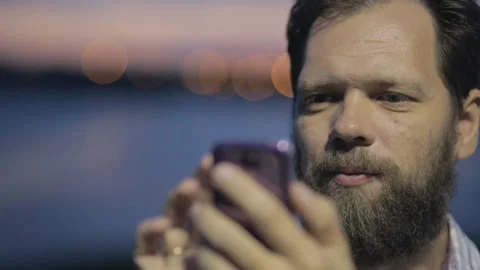 Bearded man with a smartphone in his hand on the background of the city at night Stock Footage 99138959