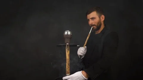 Bearded man smokes hookah and exhales smoke on a black background. Slow motion. Stock Footage 125455465