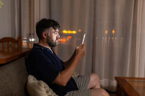 Bearded man on sofa uses digital tablet in dining room overnight Stock Photos