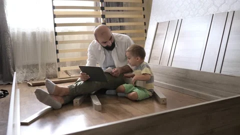 Bearded man with son sitting on the floor reading instruction in the tablet for Stock Footage 204895725