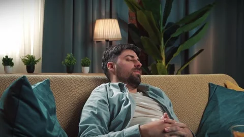 Bearded man spending time at home with fast food delivery, sits on couch and Stock Footage 305485832