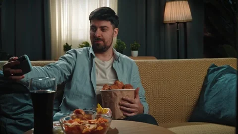 Bearded man spending time at home with fast food delivery, sits on couch holding Stock Footage 305487013