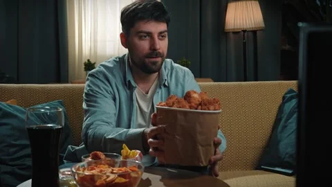 Bearded man spending time at home with fast food delivery, sits on couch Stock Footage 305488193