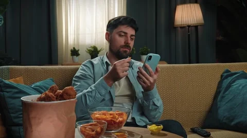 Bearded man spending time at home with fast food delivery, sits on couch Stock Footage 305492887