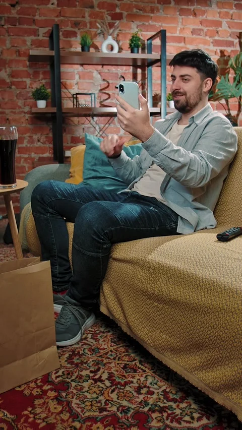 Bearded man spending time at home with fast food delivery, sits on couch talking Stock Footage 305496482