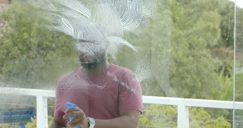 Bearded man spraying with blue bottle and squeegeeing balcony glass panel to Stock Footage 335867526