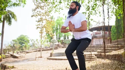 Bearded man squats hands joined in meditation outdoor Stock Footage 303963720