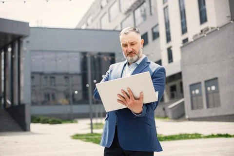 Bearded man standing and using a laptop in front of modern office Foto stock