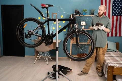 Bearded man standing and using digital tablet while repairing bicycle on st.. Stock Photos