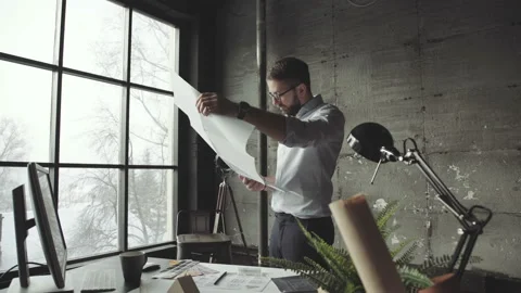 Bearded man standing faces to panoramic window and looks at blueprints Stock-Footage 87108717