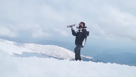 Bearded man standing in snow on top of mountain holding drone makes funny Video stock 249048102