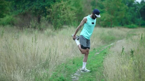 Bearded man stretching quadriceps pulling foot behind on grassy trail outdoors Stock Footage 313951465
