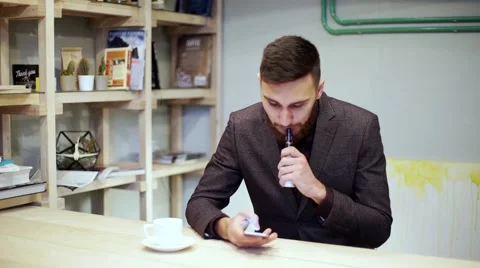 Bearded man in suit is smoking e-cigarette vape, chatting by smart phone Stock Footage 56891583