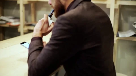 Bearded man in suit is smoking e-cigarette vape, chatting by smart phone Stock Footage 56891656
