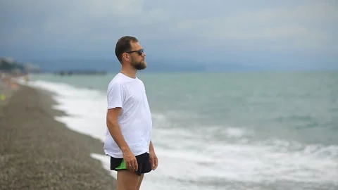 Bearded man in sunglasses on the beach looking at the sea waves. Stock Footage 116170111