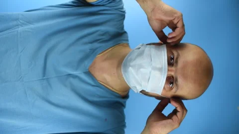 Bearded man take off a face mask on a blue background, vertical video Stock Footage 141746060