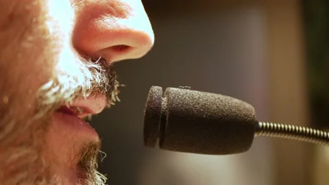 Bearded man talking into a microphone. Dark background. 스톡 동영상 166622083