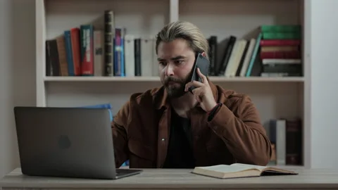 Bearded man talking on mobile and typing on laptop Stock Footage 172525464