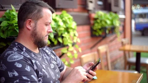 Bearded man talking on the phone and chatting in a cafe on the street. 4k. Stock Footage 103923312
