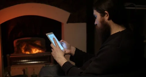 A bearded man talking on a smartphone near the fireplace Vídeos de archivo 88057897