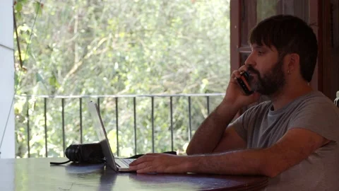 Bearded man talking on the smartphone while working with a laptop Stock Footage 139611848