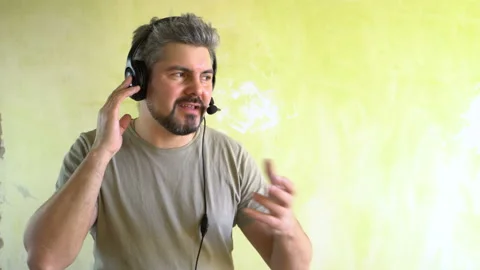 A bearded man is talking through headphones with a microphone on his head Stock Footage