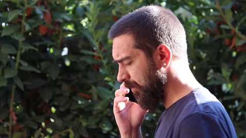 A bearded man talks on the phone behind a hedge with a serious face Stock Footage 139064602