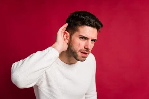Bearded man touching head on red background pretending to listening something Stock Photos