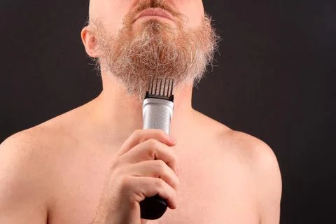 Bearded man with trimmer to adjust beard in hand Stock Photos