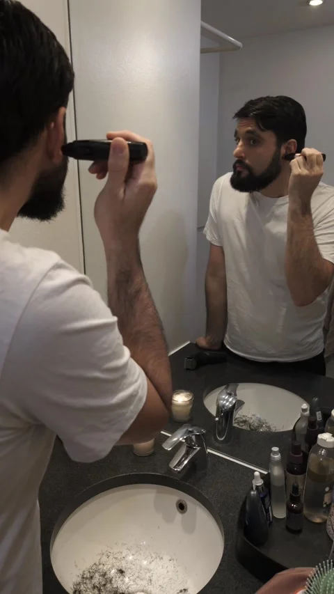 Bearded man trimming his ears with electric trimmer in bathroom mirror Video stock 335638253
