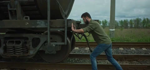 Bearded man trying to push oil tank train, on railways Stock Footage 201141893