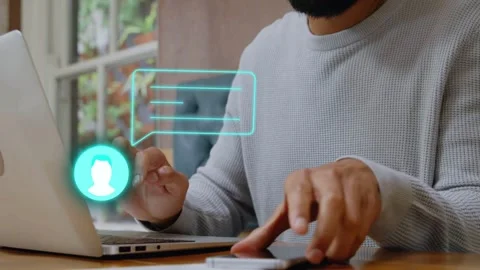 Bearded man typing on laptop at tech desk, replying to incoming teal chat, Stock Footage 334703691