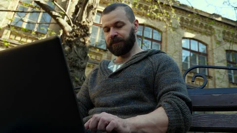 The bearded man   typing text on a laptop in the park. Stock Footage 88782749