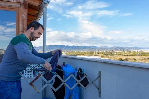 Bearded man upset while doing the housework of hanging clothes on the terrace Stock Photos