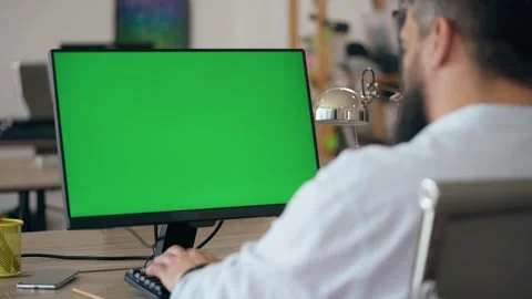 Bearded Man Uses Desktop Computer with Green Mock-up Screen In Office Stock Footage 241667459