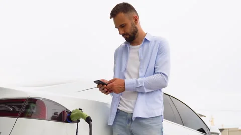 Bearded man uses a mobile application to control the battery of an electric car Stock Footage 251764004