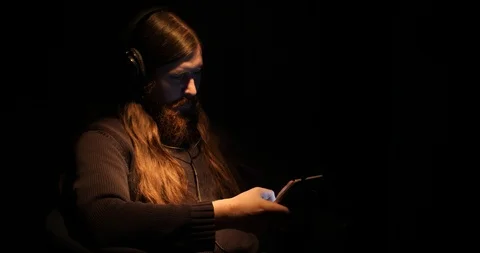 Bearded man uses a tablet and listens music in a dark room Stock Footage 88060051