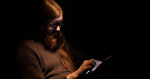 Bearded man uses a tablet in a dark room Stock Footage 88059961