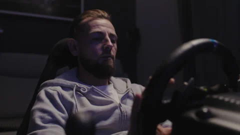 A bearded man using a driving simulator at home and looking at the steering.. Stock-Footage 258387984