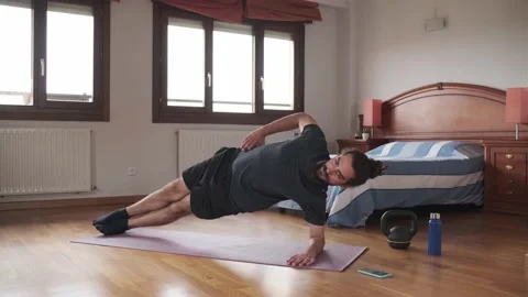 Bearded man using his mobile phone to exercise at home doing side plank. Stock Footage 158487937