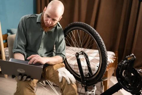 Bearded man using laptop to watch online bicycle repair tutorial at home. B.. 스톡 사진