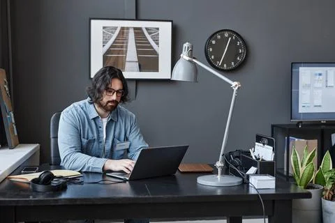 Bearded man using laptop working at desk in office interior in dark colors Stock-Fotos